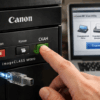 Рука нажимает кнопку "СКАН" на принтере Canon MF3010, подключенном к ноутбуку.