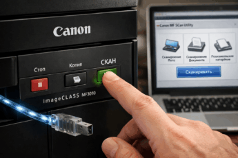 Рука нажимает кнопку "СКАН" на принтере Canon MF3010, подключенном к ноутбуку.